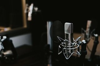 An independent artist holding a pen, writing lyrics in a physical notebook with studio monitors and a microphone nearby.