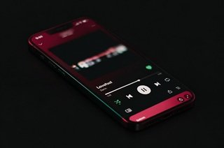 A smartphone lying on a dark surface displaying the Spotify mobile music player app screen.