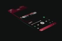 A smartphone lying on a dark surface displaying the Spotify mobile music player app screen.