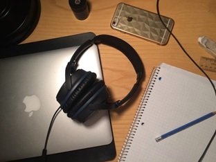 Over-ear studio headphones resting on a laptop next to a notepad for music split sheets and PRO song registration.