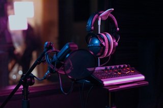 A clean home recording studio desk featuring an audio interface, studio headphones, and a condenser microphone on an adjustable boom arm.