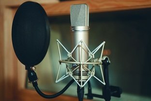 A condenser microphone on a boom stand with a mesh pop filter set up in a home studio recording space.