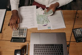 Person counting money beside a laptop, calculator, and financial documents.