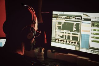 Music producer wearing headphones while working on a computer in a recording studio.