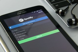 Spotify app displayed on a mobile device next to earphones and a laptop.