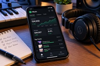 Smartphone resting on a studio desk next to headphones displaying music streaming data and listener analytics.